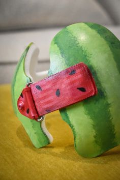 a watermelon shaped sculpture with a red belt around it's neck on a yellow surface