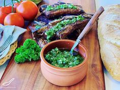 a wooden cutting board topped with meat covered in pesto next to bread and tomatoes