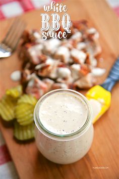 a glass jar filled with white bbq sauce sitting on top of a wooden cutting board