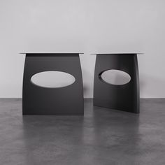 two black and white tables sitting next to each other on a cement floor in front of a wall