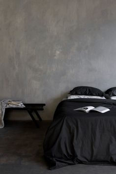 a bed with black sheets and pillows next to a wall that has a book on it