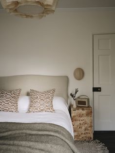 a bed with white sheets and pillows in a bedroom next to a door that has a clock on the wall