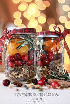 two jars filled with fruit and nuts on top of a white table next to a christmas tree