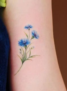 a small blue flower tattoo on the right side of the leg, with green leaves