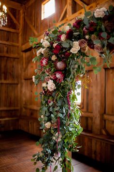 an arrangement of flowers and greenery is hanging from a pole in the middle of a room