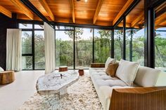 a living room with couches, tables and windows overlooking the trees in the distance