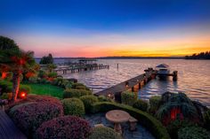 the sun is setting at the end of the pier on the water with trees and bushes around it