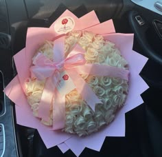 a bouquet of white roses wrapped in pink ribbon sits on the dashboard of a car