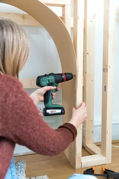 a woman using a power drill to attach a piece of wood on the wall in front of her