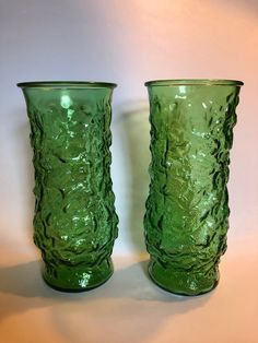 two green glass vases sitting next to each other on a white tableclothed surface