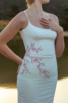 a woman wearing a white dress with pink flowers on it and her hands on her chest