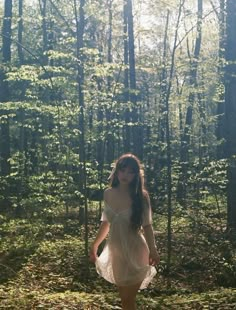 a woman in a white dress is walking through the woods with her hands on her hips