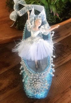 a ballerina doll sitting on top of a blue ballet shoe with white and silver sequins