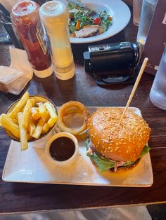 a plate with a hamburger and fries on it sitting on a table next to drinks