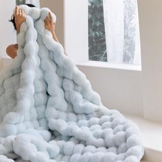 a woman laying on top of a pile of fluffy white blankets in front of a window