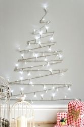 a small christmas tree with white lights in the corner next to a birdcage