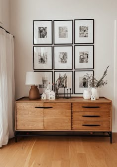 a wooden dresser sitting next to a window with pictures on the wall above it and a lamp