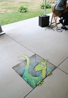 a drawing of a green dragon on the ground next to a man sitting in a chair