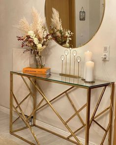 a console table with flowers and candles on it in front of a mirror that is next to a wall