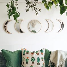 a couch with pillows and plants hanging on the wall next to it is surrounded by three crescent shaped mirrors