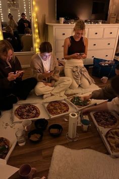 several people sitting on the floor eating pizza and looking at their phones