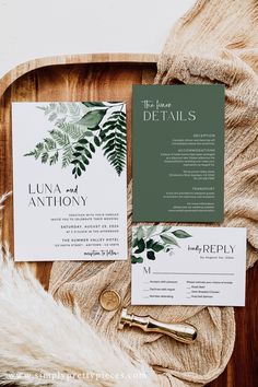 the wedding stationery is laid out on a wooden tray with greenery and gold accents