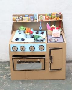 a cardboard toy stove and oven with food on the burners, in front of a white wall