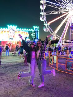 two women pose for a photo in front of an amusement park with ferris wheel at night