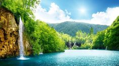 there is a large waterfall in the middle of this lake with blue water and green trees on both sides