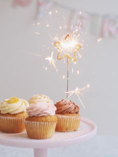 three cupcakes on a cake stand with sparklers