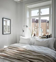 a bed with white sheets and pillows next to a window