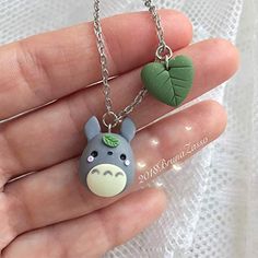 a hand holding a tiny animal necklace with two charms on it's sides and a heart shaped leaf hanging from the other side