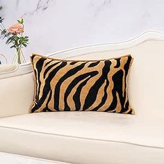 a zebra print pillow sitting on top of a white couch next to a vase with flowers