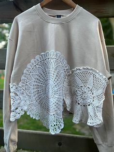 an old sweater with crochet on it hanging from a clothes line in front of a wooden fence