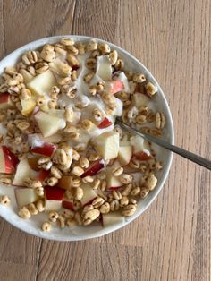 a bowl filled with fruit and nuts on top of a wooden table next to a spoon