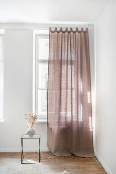 a room with white walls and wooden floors has a small table in front of the window