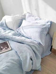 an unmade bed with blue sheets and pillows on the floor next to a window