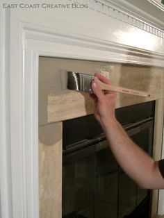 a man is painting a fireplace with white paint on the mantle and holding a brush