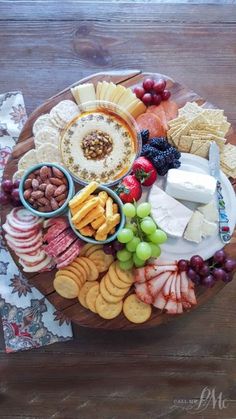 a wooden platter filled with cheese, crackers and fruit