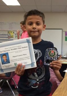 a young boy holding up a certificate in front of his face and smiling at the camera