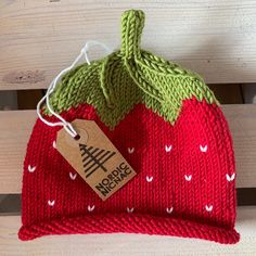 a knitted strawberry hat sitting on top of a wooden bench with a tag attached to it