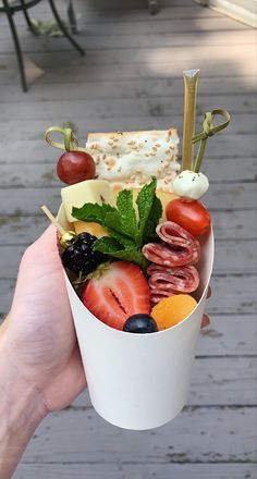 a person holding up a cup filled with fruit and cheese