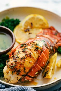 a plate with lobster, broccoli and lemon wedges on it next to a dipping sauce