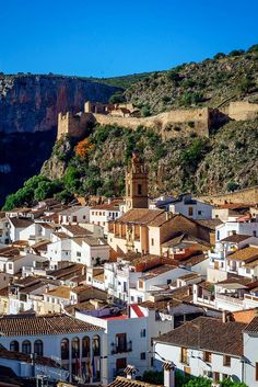 an old town with mountains in the background and blue sky above it, surrounded by white buildings