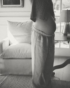 a black and white photo of a baby standing in front of a living room window