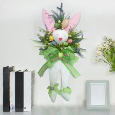 a stuffed animal hanging from the side of a wall next to flowers and books on a shelf