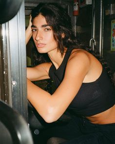 a beautiful young woman in a black top leaning against a metal wall with her hand on her head