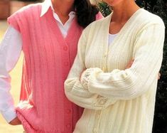 two women standing next to each other in front of a tree wearing sweaters and hats