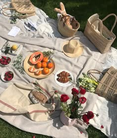 an outdoor picnic is set up on the grass with flowers and fruit in bowls, bread baskets, and straw hats