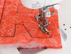 the sewing machine is next to an orange piece of fabric that has been sewn